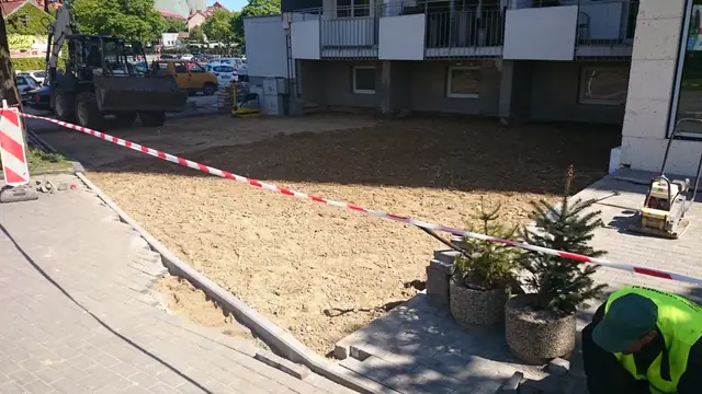 Przygotowane piaszczyste podłoże odgrodzone taśmą ostrzegawczą przed wejściem do hotelu, obok donice ze świerkami