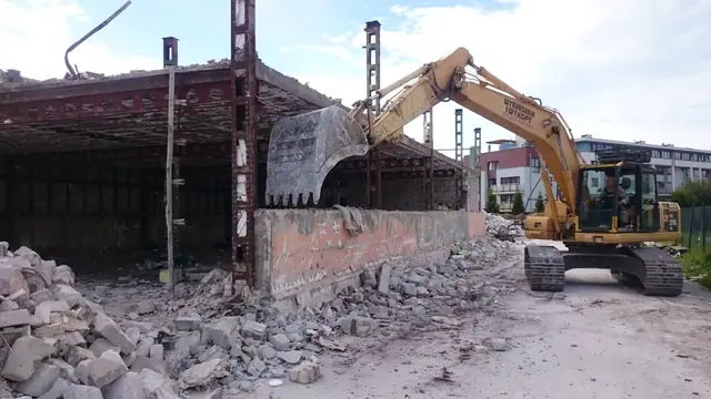 Koparka z młotem hydraulicznym rozbija fragment ściany hali magazynowej