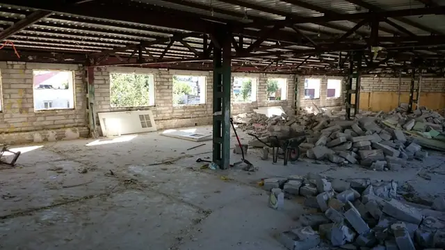 Wnętrze hali ze stalową konstrukcją dachu i stertami gruzu po rozbiórce ścian