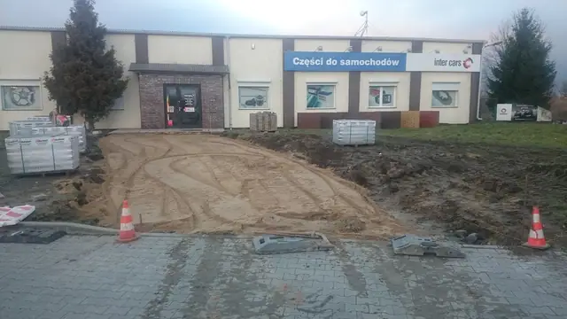 Wyrównana podsypka piaskowa pod chodnik przed wejściem do Inter Cars, obok palety kostki brukowej