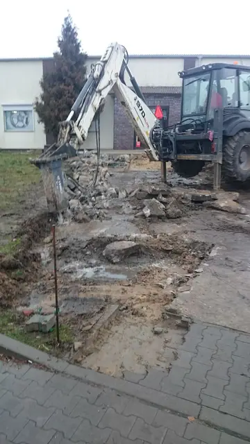 Koparko-ładowarka z młotem skuwa stary beton przed wejściem do sklepu Inter Cars w Kołobrzegu
