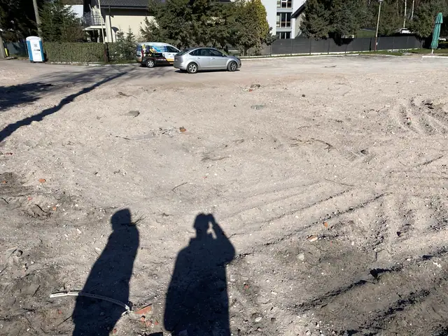 Wyrównany plac po zakończonej rozbiórce ośrodka Jantar w Dźwirzynie, w tle zaparkowane samochody