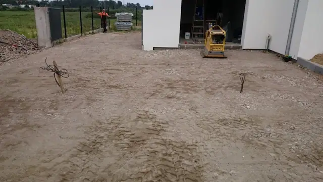 Wyrównana piaszczysta nawierzchnia przed garażem z zagęszczarką, przygotowanie pod kostkę