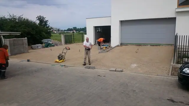 Robotnicy zagęszczarką przygotowują podsypkę pod kostkę brukową przed garażem domu jednorodzinnego