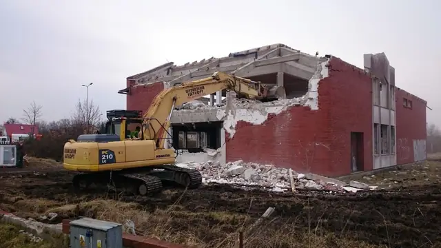 Koparka gąsienicowa Komatsu PC210 rozbiera ceglane ściany budynku przy ul. Jasnej w Kołobrzegu