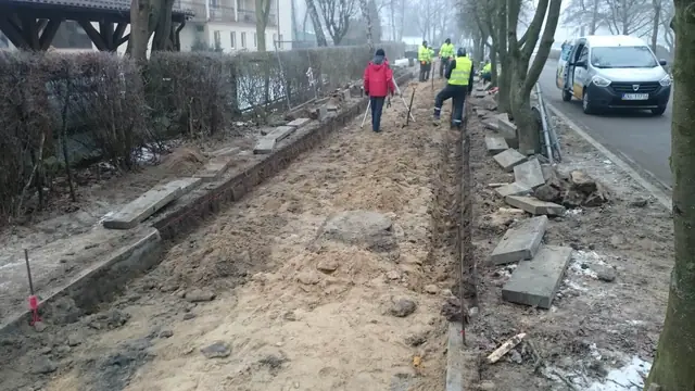 Robotnicy formują krawężnikiem obrzeże chodnika wzdłuż ulicy, obok resztki starej nawierzchni