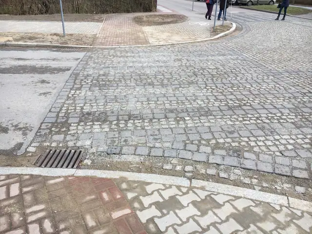 Zbliżenie na kratkę ściekową osadzoną w nawierzchni z kostki granitowej i klinkierowej