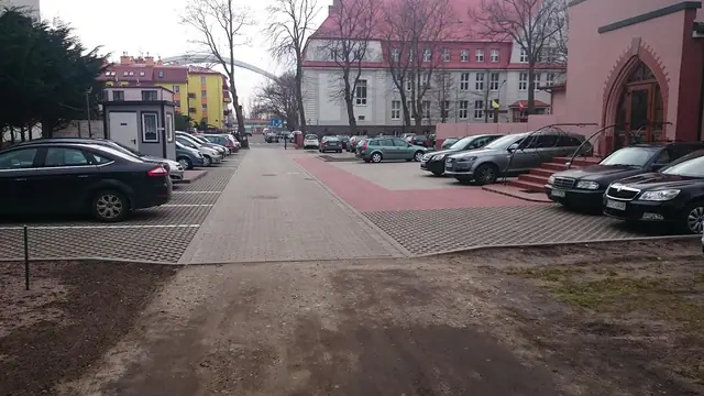 Aleja z czerwonej kostki brukowej prowadząca do parkingu przy kościele, w tle ratusz