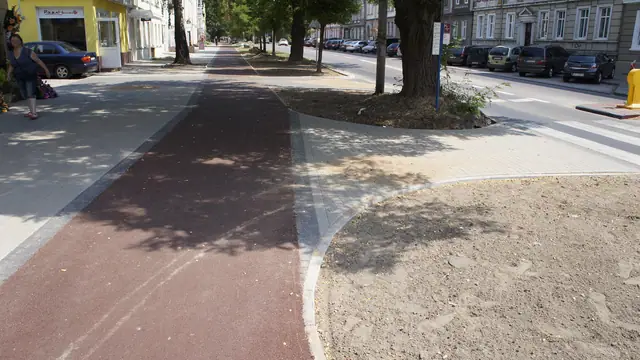 Czerwona nawierzchnia ścieżki rowerowej wzdłuż alei drzew w centrum Koszalina