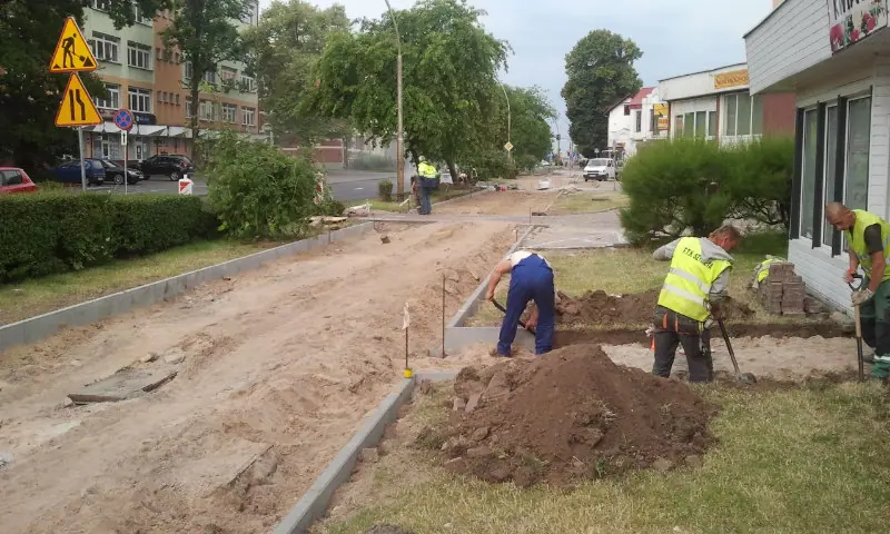 Robotnicy kopią rów pod krawężnik na zieleńcu przy chodniku podczas budowy ścieżki rowerowej w Koszalinie