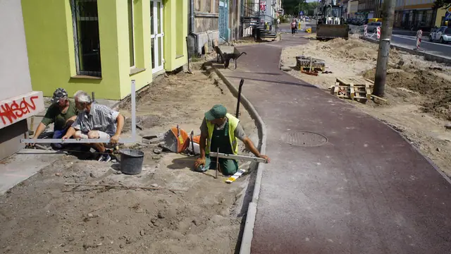 Robotnicy układają krawężnik przy czerwonej ścieżce rowerowej obok kamienicy w Koszalinie