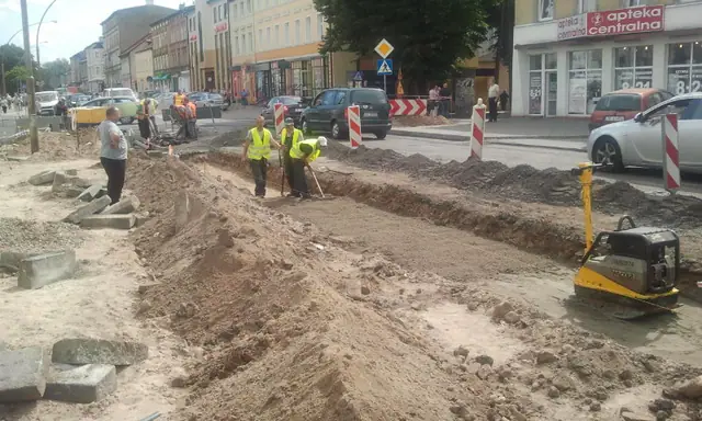 Wykop pod ścieżkę rowerową wzdłuż ulicy handlowej, robotnicy obsługują zagęszczarkę w Koszalinie