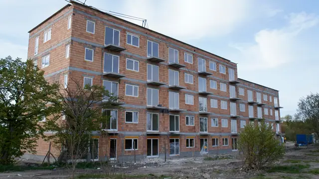 Budynek z czerwonej cegły bez tynku widziany z placu budowy, gruz w tle