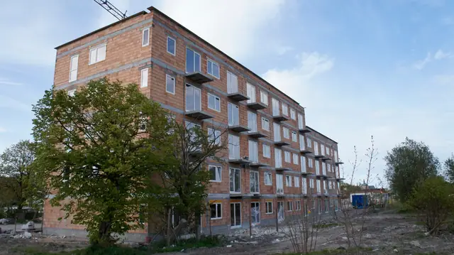Budynek z czerwonej cegły widziany z boku wśród zieleni, drzewo na pierwszym planie
