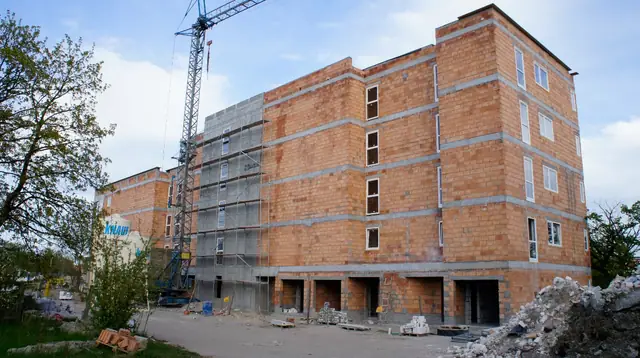 Wysoki budynek z czerwonej cegły z widocznym żurawiem wieżowym, otoczony ogrodzeniem