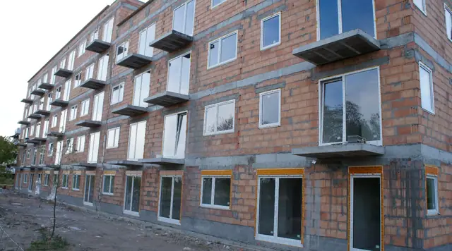 Kolejny narożnik budynku z czerwonej cegły z oknami PCV i wystającymi balkonami
