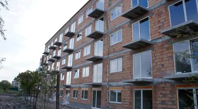 Narożnik budynku z czerwonej cegły z zamontowanymi oknami PCV i balkonami