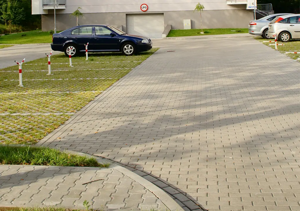 Parking z kostki brukowej przed gotowym budynkiem mieszkalnym, zaparkowany granatowy samochód