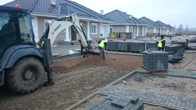Koparka Terex ustawia palety szarej kostki brukowej przy rzędzie domów jednorodzinnych