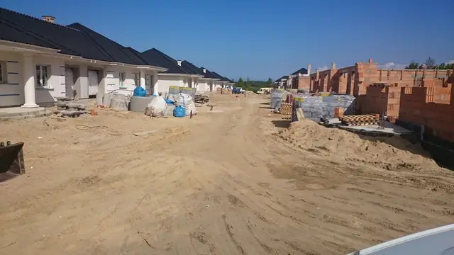 Piaszczysta droga dojazdowa między gotowymi białymi domami z materiałami budowlanymi na poboczu