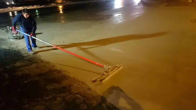 Pracownik zaciera świeżą nawierzchnię betonową długą łatą w nocy