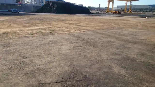 Wyrównany żwirowy plac składowy MEC z widocznymi dźwigami przemysłowymi w tle