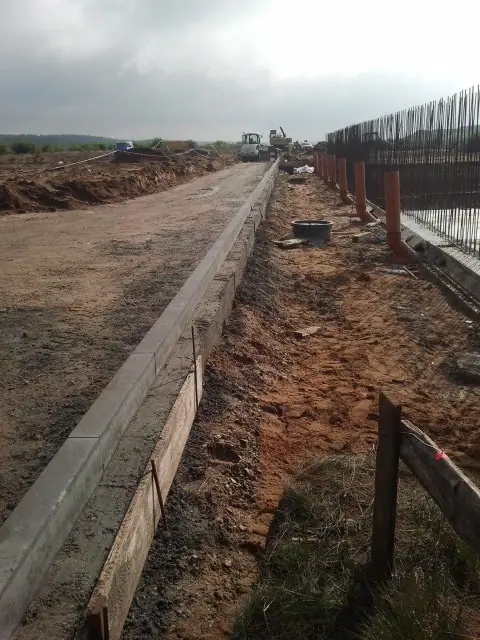 Długi odcinek betonowego krawężnika formowany drewnianymi palikami wzdłuż granicy działki