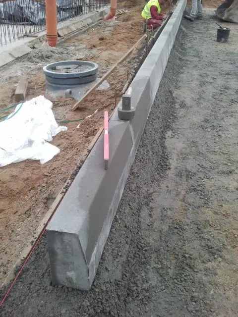 Świeżo wylany betonowy element krawężnika wyrównywany przy pomocy różowej łaty pomiarowej