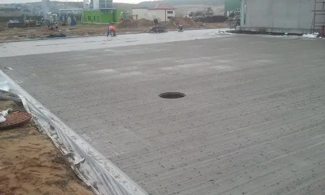 Szeroki widok ukończonej płyty betonowej ze studzienką rewizyjną i pasem izolacji na krawędzi