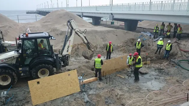 Koparko-ładowarka przy betonowaniu muru oporowego w szalunkach z płyt OSB, w tle most przy molo w Kołobrzegu