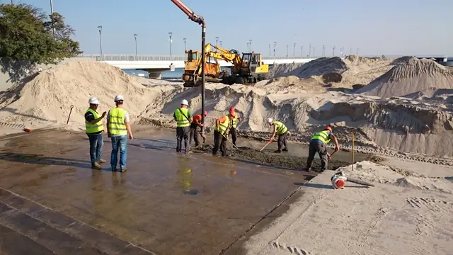 Robotnicy w kamizelkach odblaskowych betonują schody pompą do betonu na plaży przy molo w Kołobrzegu