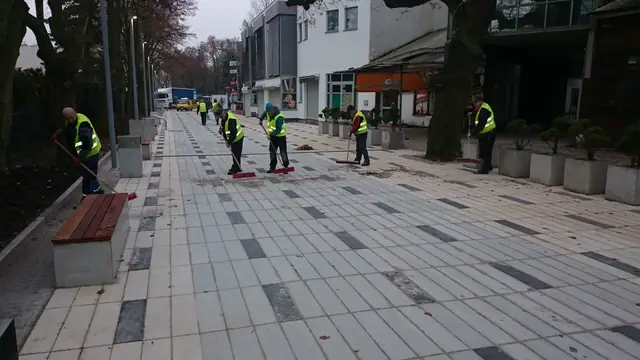 Robotnicy czyszczą zamiatarkami gotową nawierzchnię chodnika przed sklepami przy molo w Kołobrzegu