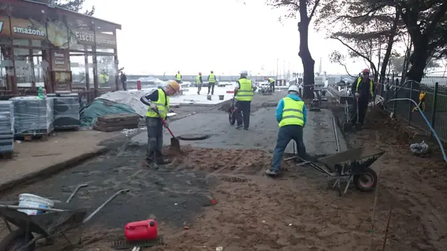 Koparko-ładowarka za tymczasowym ogrodzeniem podczas prac przy chodniku ulicznym w centrum Kołobrzegu