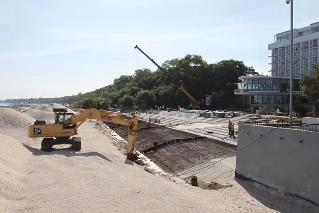 Dwie koparki gąsienicowe przy prefabrykowanych elementach betonowych i dźwigu na placu budowy przy molo