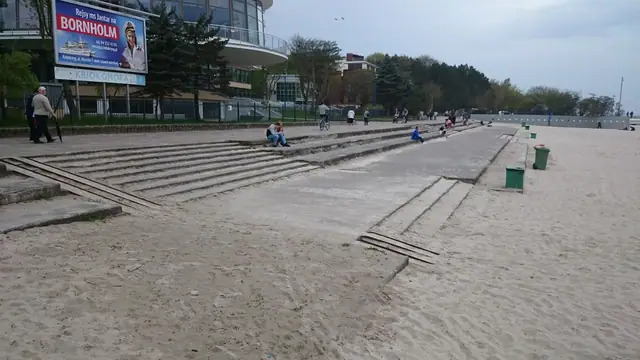 Ludzie siedzą na starych betonowych schodach prowadzących na plażę przy molo w Kołobrzegu