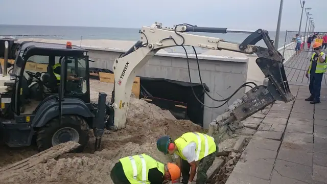 Minikoparka z młotem hydraulicznym pracuje przy murku oporowym pod nadzorem robotników przy molo w Kołobrzegu