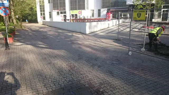 Robotnik montuje tymczasowe ogrodzenie budowy na starym placu przed rozpoczęciem prac przy molo w Kołobrzegu