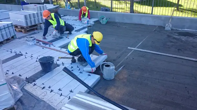 Robotnicy montują płyty chodnikowe na tarasowej konstrukcji przy murze oporowym przy molo w Kołobrzegu