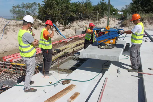 Robotnicy montują prefabrykowaną płytę betonową dźwigiem podczas budowy schodów przy molo w Kołobrzegu