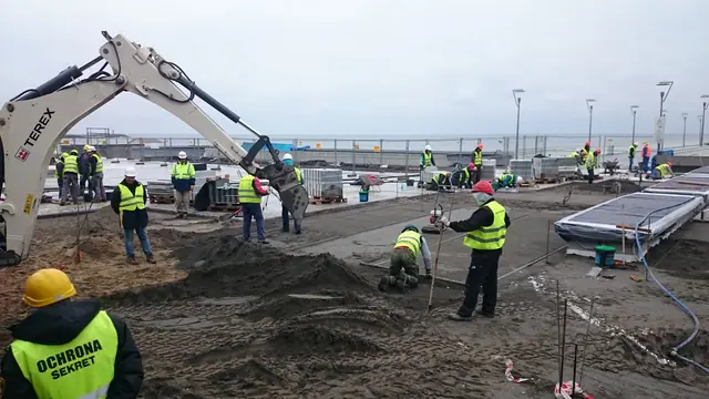 Robotnicy pracują nocą przy sztucznym oświetleniu podczas prac wykończeniowych placu przy sklepach przy molo