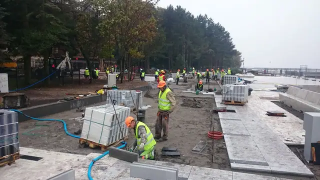 Robotnicy przy paletach z kostką brukową na terenie przygotowanym pod nowy chodnik przy molo w Kołobrzegu
