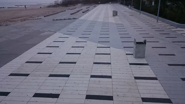 Wieczorna panorama ukończonego placu przy molo w Kołobrzegu z pasami ciemnych płyt i koszem na śmieci