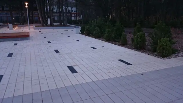 Ukończony plac przy molo w Kołobrzegu z ozdobnymi krzewami w otoczeniu grysu i drewnianą ławką o zmierzchu