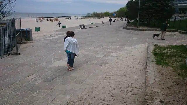 Kobieta idzie piaszczystą plażą wzdłuż tymczasowego ogrodzenia przed rozpoczęciem prac przy molo w Kołobrzegu