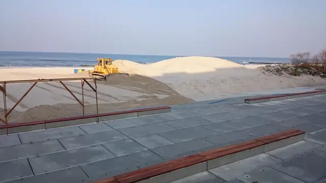 Ułożone szare płyty chodnikowe na plaży obok stalowej konstrukcji w trakcie budowy promenady przy molo
