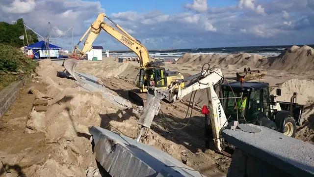 Koparka z młotem wyburzeniowym rozbija betonowe krawężniki obok ładowarki na placu budowy przy molo