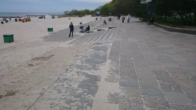 Stara nawierzchnia z płyt betonowych na piasku plaży z ludźmi odpoczywającymi przy molo w Kołobrzegu