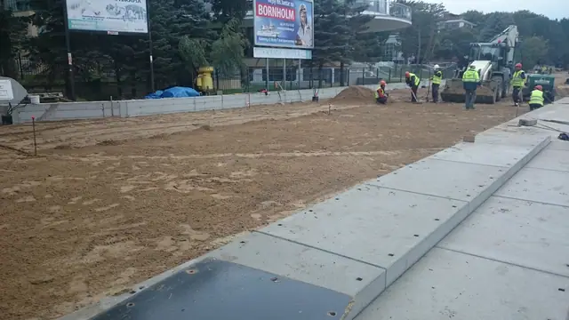 Pracownik z tyczką geodezyjną na tle prac betoniarskich w obłoku pyłu przy molo w Kołobrzegu