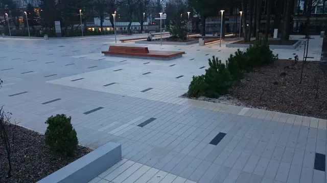 Plac przy molo w Kołobrzegu wieczorem, widok w stronę drzew i oświetlonych budynków w oddali
