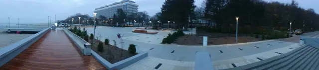 Widok z góry o zmierzchu na drewniany pomost prowadzący przez plac w stronę hotelu przy molo w Kołobrzegu